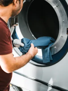Homem a colocar tecido azul na máquina de lavar roupa