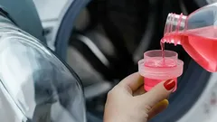 Pessoa a colocar detergente líquido rosa na máquina de lavar roupa.